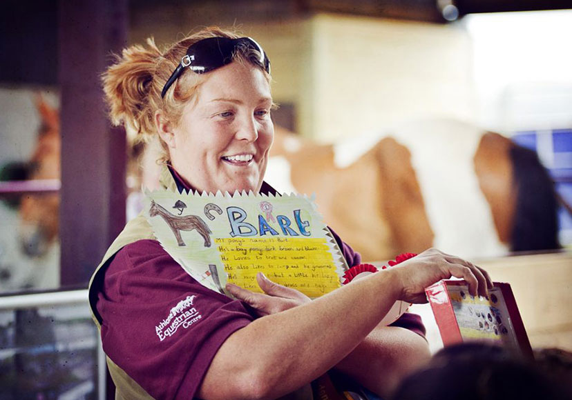 Worker showing child's artwork at Athlone Equestrian Centre.